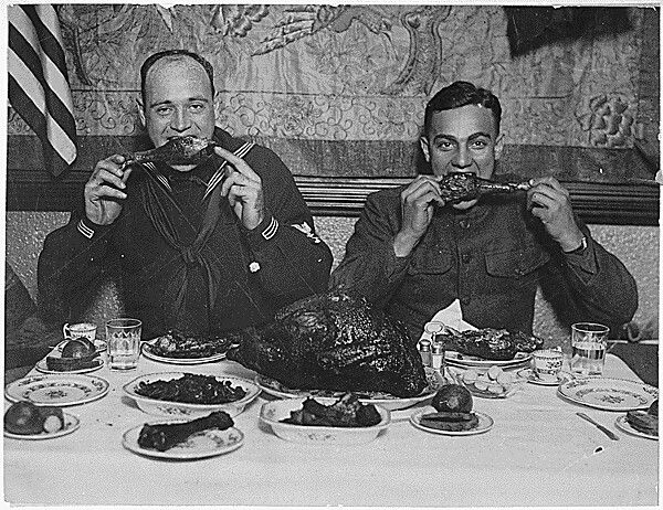 Two American military servicemembers eat turkey during a large Thanksgiving meal.