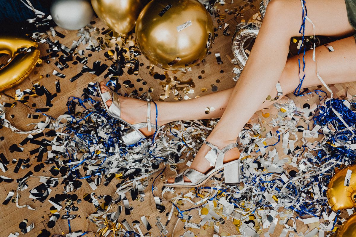 A women in heels celebrates new years eve with confetti and balloons.