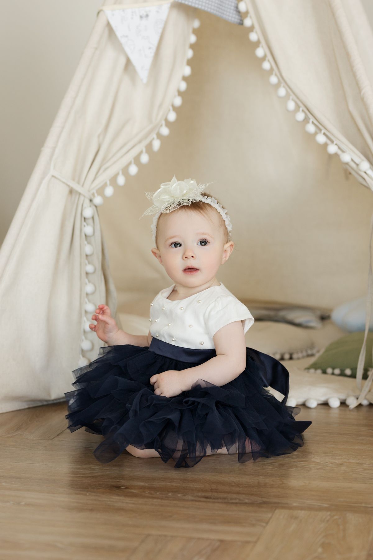 A cute baby sits while wearing a dress.