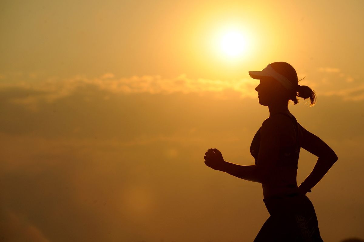 The silhouette of someone running against a bright yellow sky with the sun in the background.