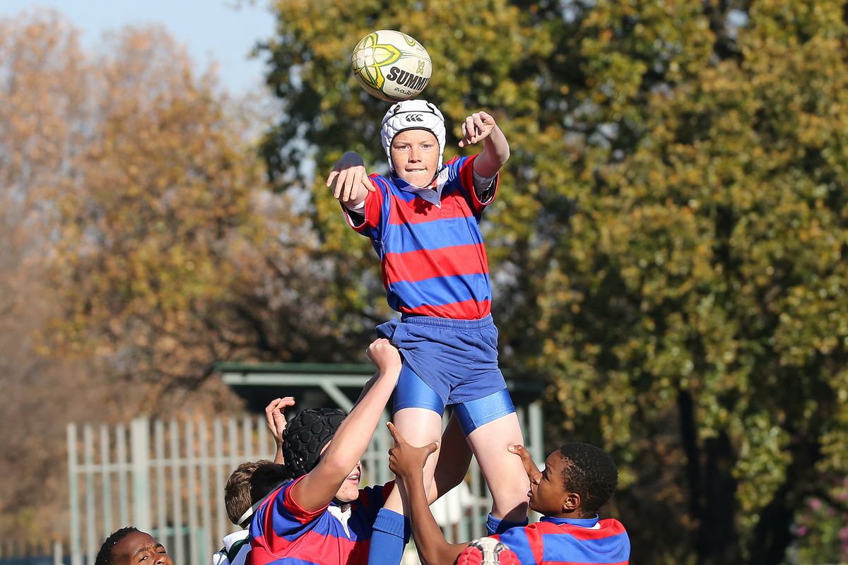 A kid is lifted to play rugby by his teammates wearing red and blue stripes.