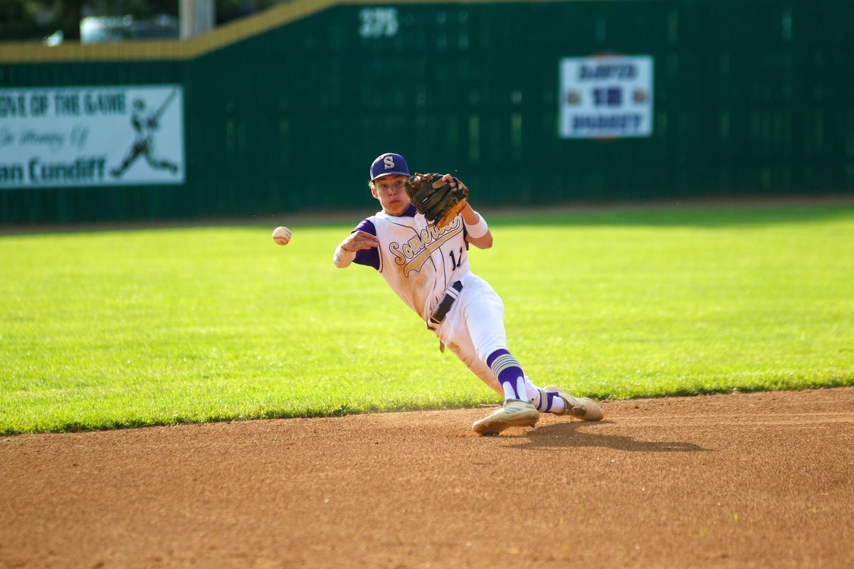 A baseball player throws a ball toward the camera as they lose their balance.