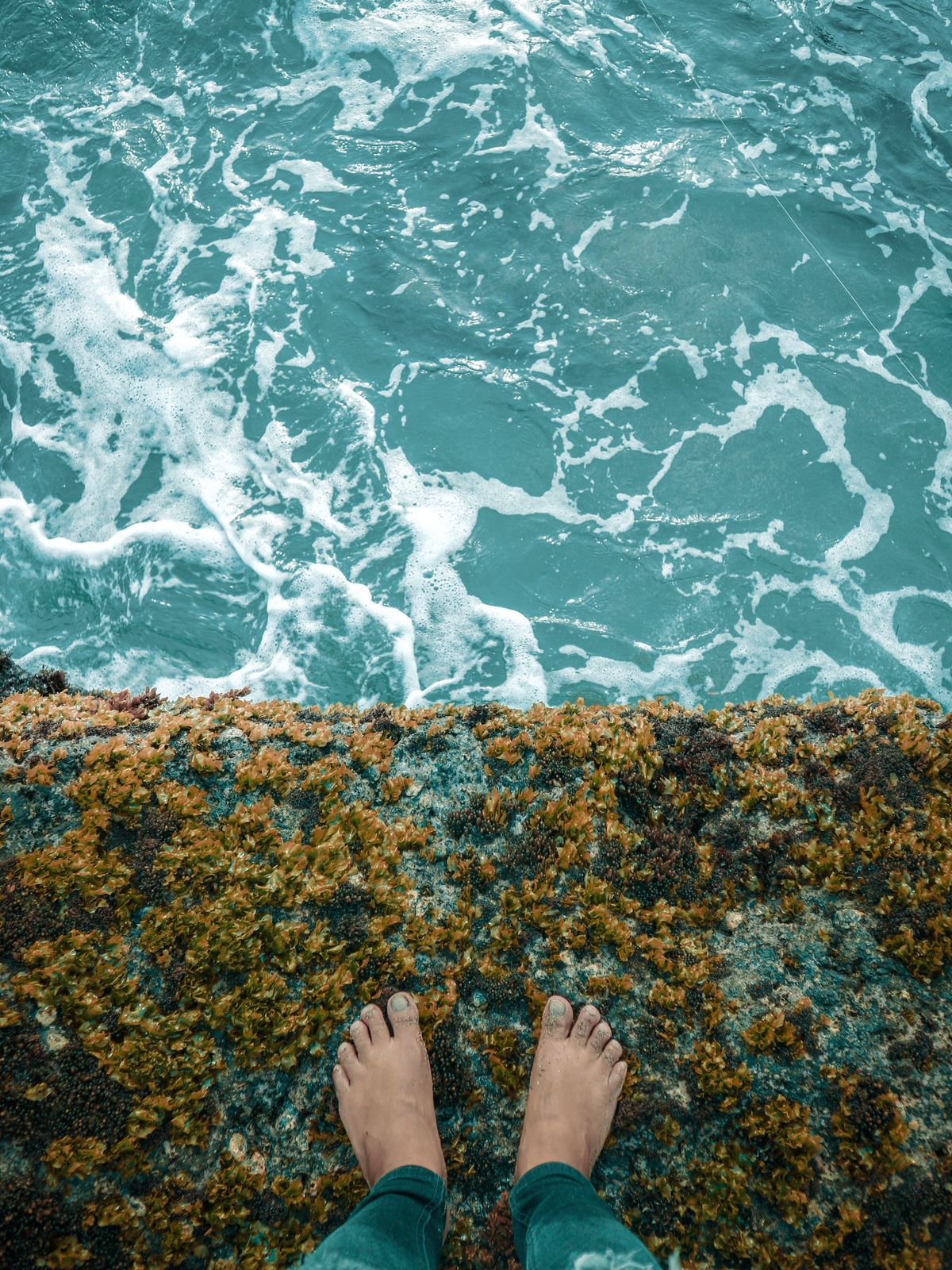 Sandy bare feet on a rocky escarpment at the edge of the ocean.